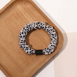 Close-up of grey polka dot scrunchie with black acrylic detail on a wooden tray