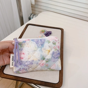 Detail of a floral quilted pouch featuring a purple braided zipper pull and logo tag