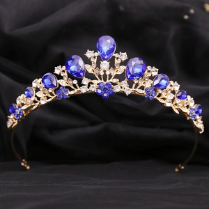 Close-up of golden crown with blue teardrop gemstones and rhinestones on black velvet