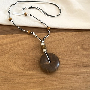 Macro shot of dark brown resin wood pendant on a black and white woven rope chain necklace