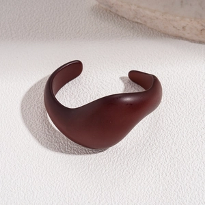 Macro detail of dark reddish-brown acrylic cuff with minimalist organic curved lines
