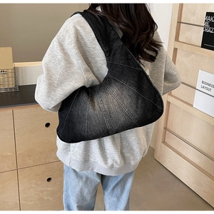 Détail du sac croissant en denim noir avec délavage vintage et coutures radiales au porté