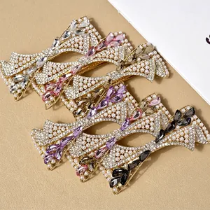Elegant gold bow hair clip with pearls and multicolored marquise crystals on a warm beige background