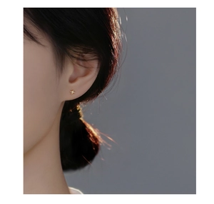 Close-up of golden eight-pointed star earrings with zircons worn on model ear