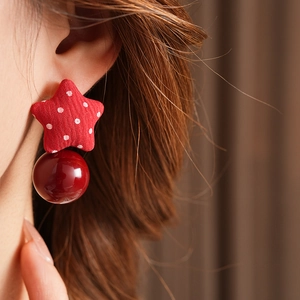 Close-up of star-shaped fabric stud earring with a glossy red pearl pendant on ear