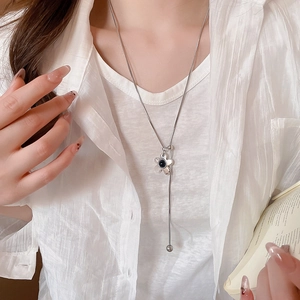Detail of silver long necklace with a black-centered flower pendant on a model wearing white
