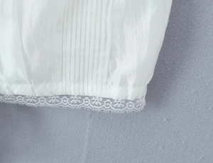 Close-up of intricate white lace edges and vertical pleated texture on a woman's camisole