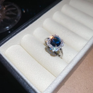 Detailed close-up of a silver ring with a blue cushion-cut gem and halo diamonds