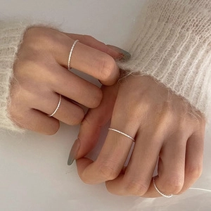 Close-up of minimalist silver rings stacked on fingers with a cozy knit sweater sleeve