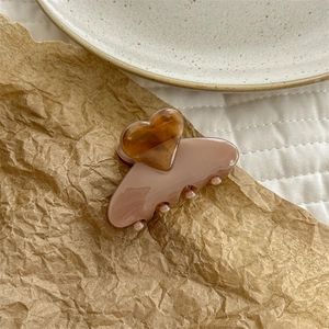 Detail of elegant pink acetate hair claw clip with a small amber heart on paper