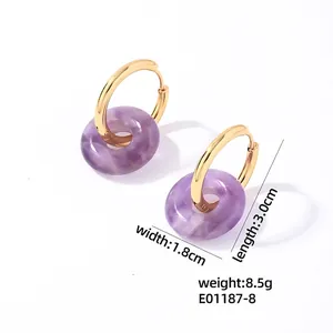 Détail de boucles d'oreilles créoles dorées en acier avec pendentifs pierre violette
