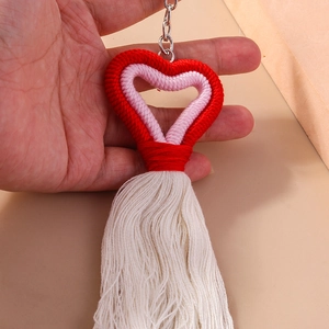 Close-up of hand holding a handmade knitted heart keychain with long white cotton tassels