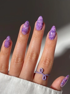 Close-up of luxury purple marble stiletto nails with sparkling diamond accents and ring