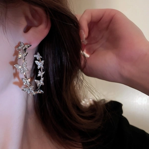 Model wearing a large silver butterfly hoop earring with shimmering rhinestones