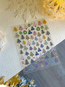 Détail de stickers à ongles de Noël avec sapins et nœuds 3D colorés sur texture blanche