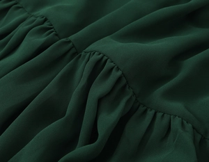 Detail view of deep green pleated chiffon fabric showing smooth texture and ruffled layers