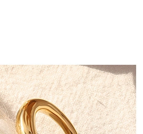 Close-up of polished 18K gold-plated chunky ring on soft beige textured fabric background