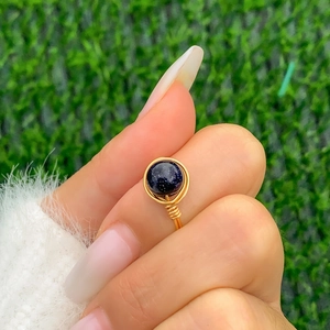 Macro shot of wire-wrapped gold ring with sparkling blue sandstone on green grass