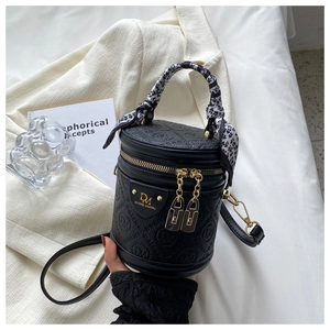 Detail of black cylinder handbag with silk scarf wrapped handle and gold logo plate