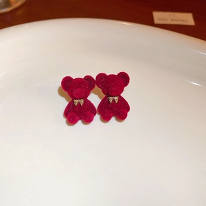 Macro shot of burgundy flocked bear earrings with gold bow details on a white tray