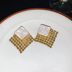 Detail of woven diamond earrings with white marble texture on a white ceramic plate