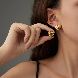 Polished gold heart earrings with sparkling star patterns shown on a model's ear