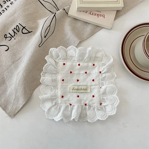 Detail of white fabric coaster with red hearts, scalloped lace edge and Sozakka label