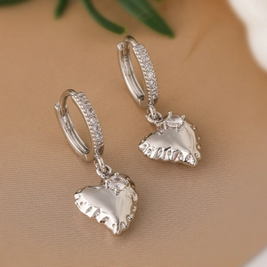 Detail of silver heart earrings with sparkling zircons on a soft beige fabric background