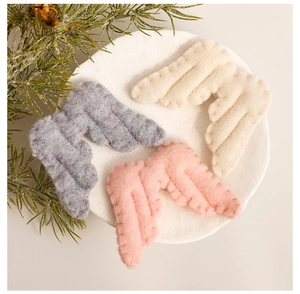 Detail of soft felt angel wings ornaments in pink, grey and cream on a round white tray