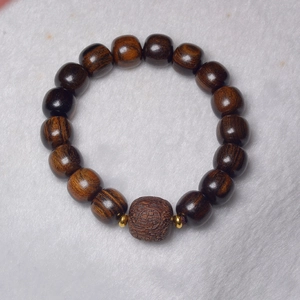 Close-up of dark brown agarwood prayer beads featuring a carved PiXiu and gold spacers