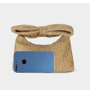 Detail of straw handbag with bow handle next to a smartphone for size reference