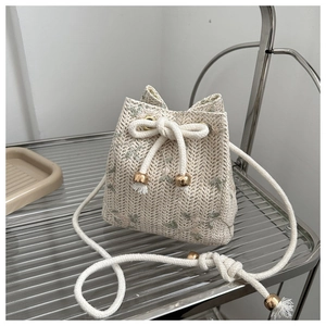 Detail of hand-woven straw bucket bag featuring delicate green floral embroidery and drawstring