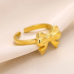 Detailed view of a golden polished bow ring on beige fabric with an adjustable band