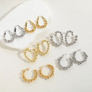 Close-up of assorted gold and silver beaded metal hoop earrings on white stone props