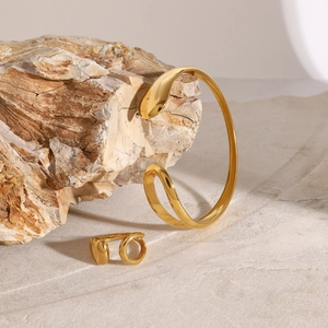 Polished gold stainless steel teardrop bangle and ring set on natural stone texture