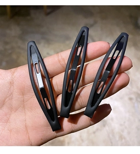 Detailed view of three large matte black metal hair clips held in hand for size context