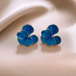 Détail macro de boucles d'oreilles fleur en émail bleu avec bords dorés et cristal