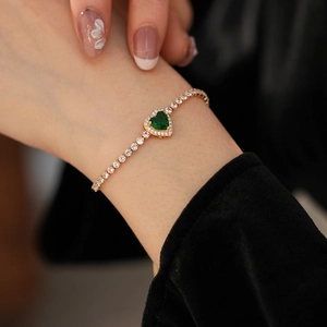 Close-up of golden heart-shaped green emerald bracelet with white zircon setting