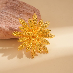 Elegant gold flower brooch with matte texture displayed on a natural red sandstone block