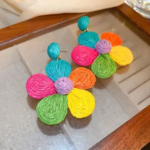 Colorful woven raffia flower drop earrings with boho petal design on wood glass display