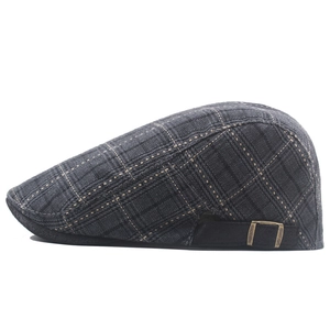 Detail of dark grey plaid beret showing fabric texture and bronze metal adjustment buckle