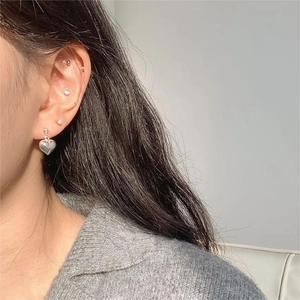 Detailed close-up of a 925 silver heart earring and pearl studs on model ear