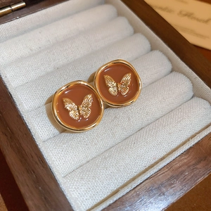 Détail de boucles d'oreilles papillon dorées en émail marron dans un coffret à bijoux en bois