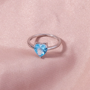 Close-up of heart-shaped blue gemstone ring with micro-pave cubic zirconia on silk