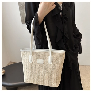 Close-up of off-white straw woven tote bag with white leather handles and detail stitching