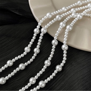 Detailed view of long geometric necklace featuring elegant white gradient pearls on dark fabric