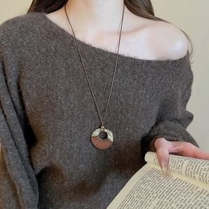 Detail of a vintage round wood and textured metal pendant necklace on a brown sweater
