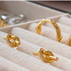 Macro shot of gold knot earrings and irregular textured ring in a beige jewelry box