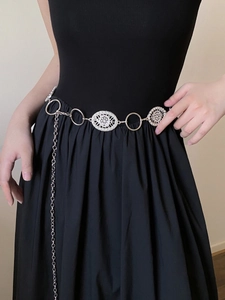 Detail of silver metal chain belt with oval cutouts and dangling charms on a model