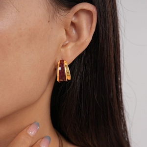 Close-up of 18k gold-plated C-shape double earrings with burgundy enamel on model